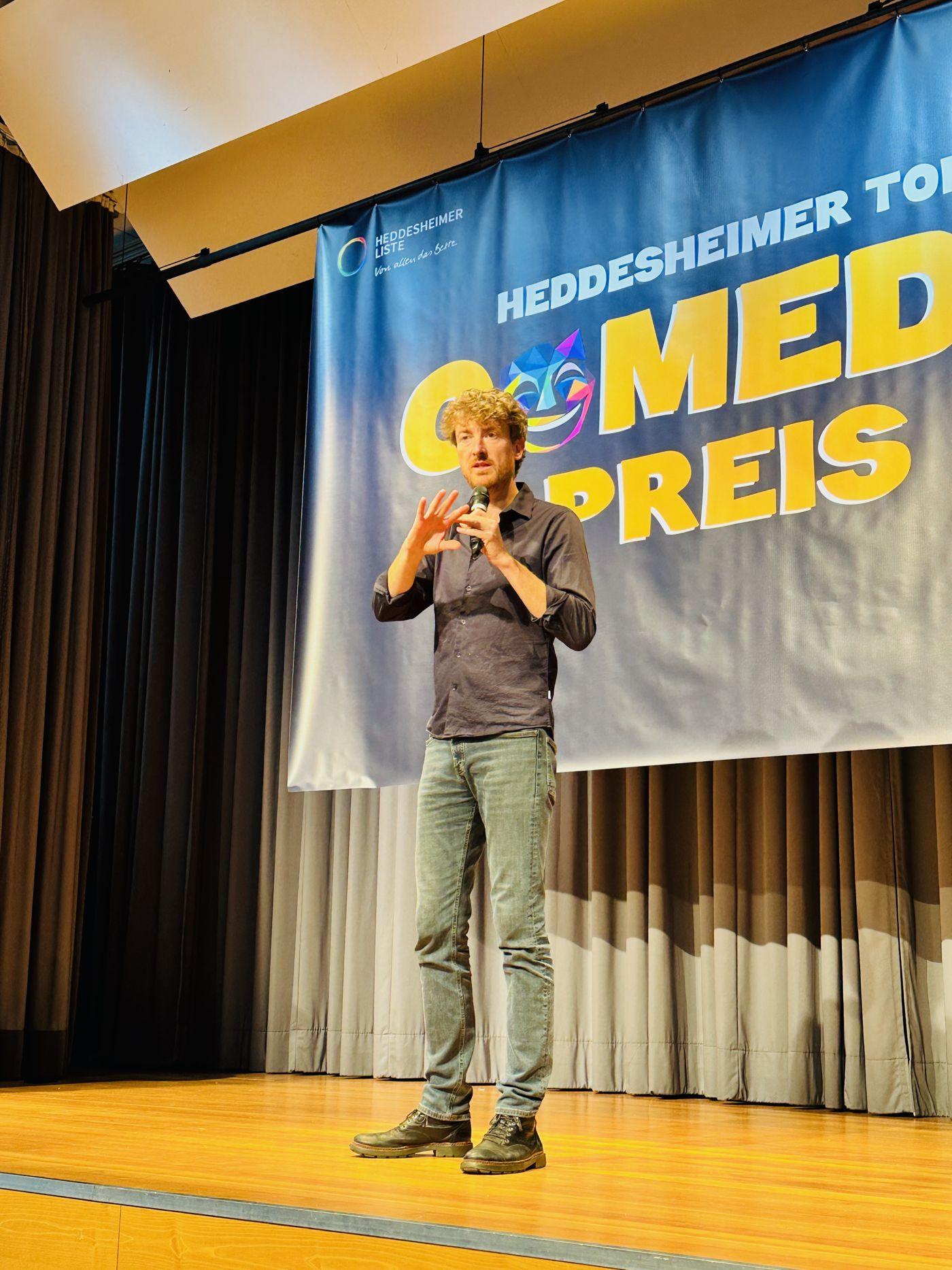 Comedian mit Mikrofon vor dem Comedypreis-Banner im Bürgerhaus